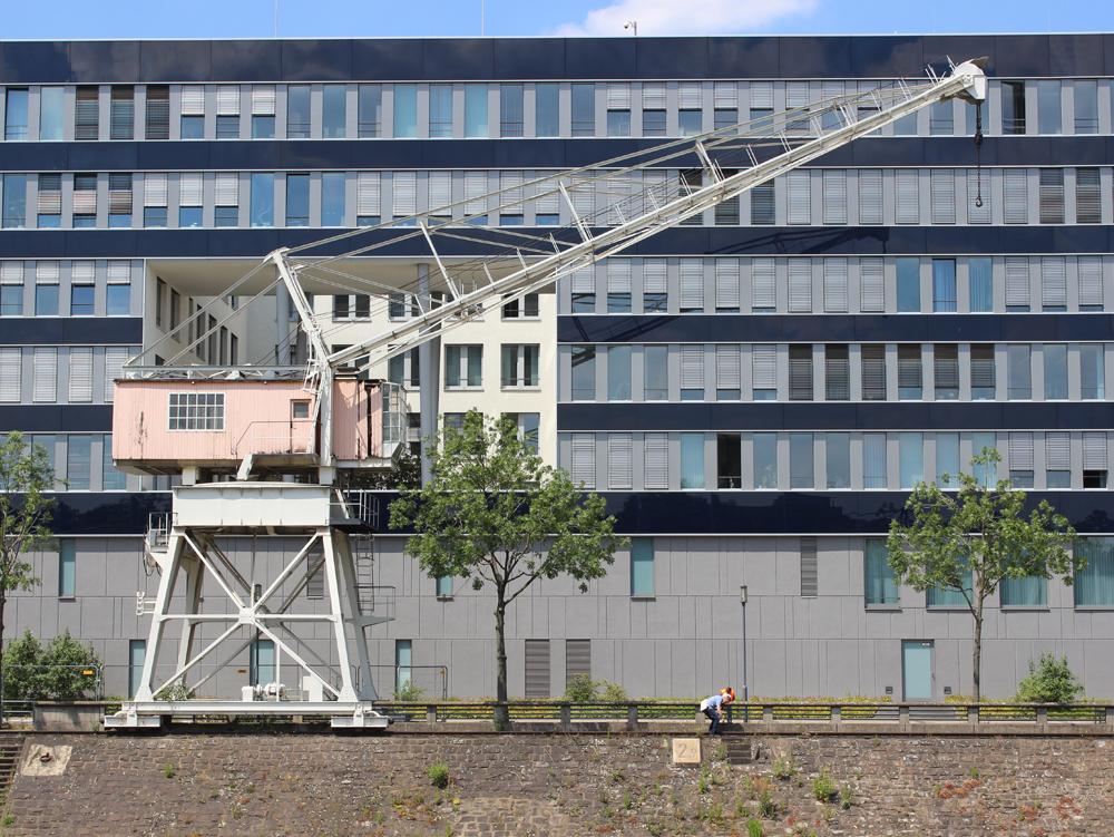 Kran vor dem Mitsubishi Power Office Ein roter Kran steht vor einem modernen, blauen Gebäude mit vielen Fenstern. Mitsubishi Power Office, Innenhafen Duisburg