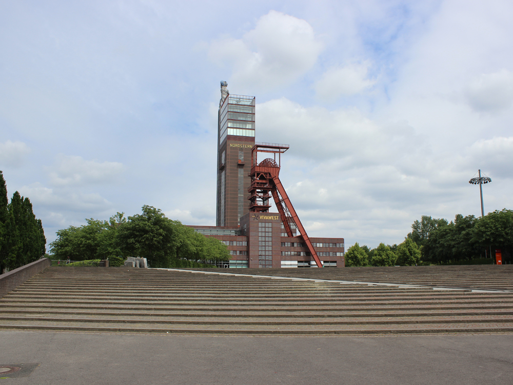 Förderturm Schacht 1 und Fördergerüst Schacht 2 Industriegebäude mit Förderturm, umgeben von Bäumen und klarem Himmel. Im Vordergrund breite große Treppe. Nordsternpark Gelsenkirchern