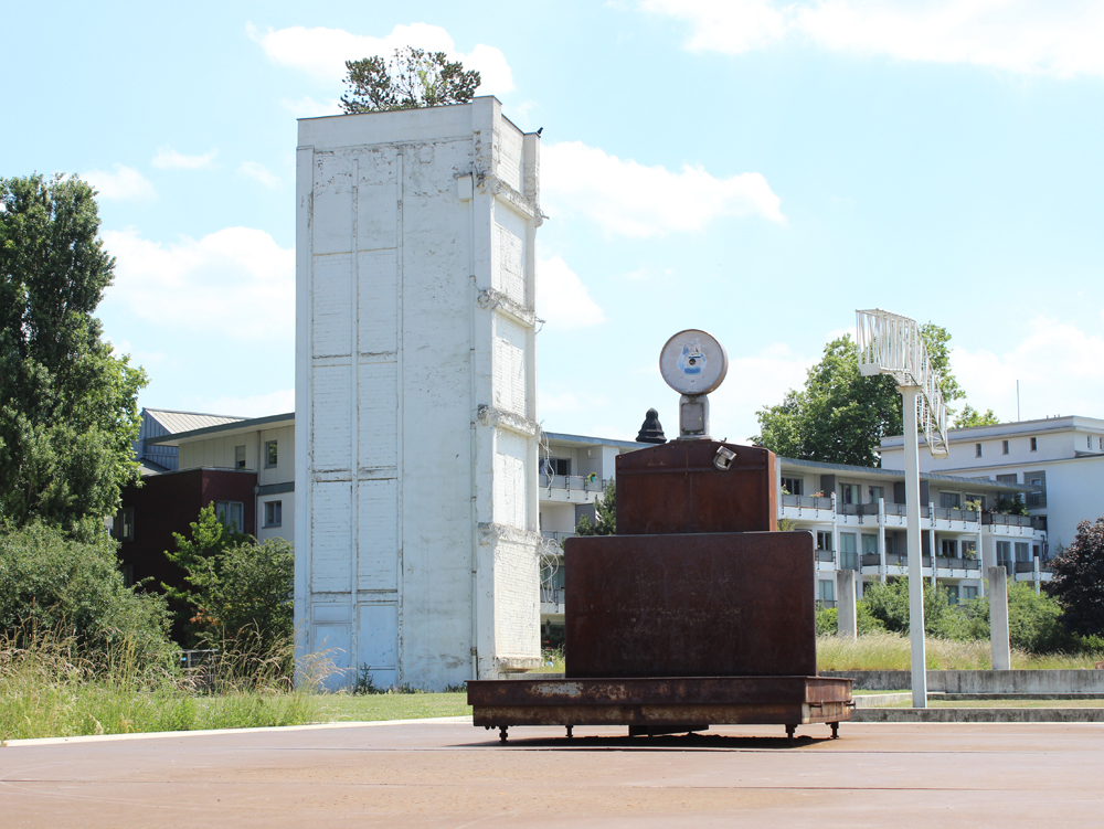 Garten der Erinnerung Skulptur mit Uhr und Metallstruktur vor Rest von ehemaligem Gebäude in einer grünen Umgebung. Innenhafen Duisburg, Garten der Erinnerung