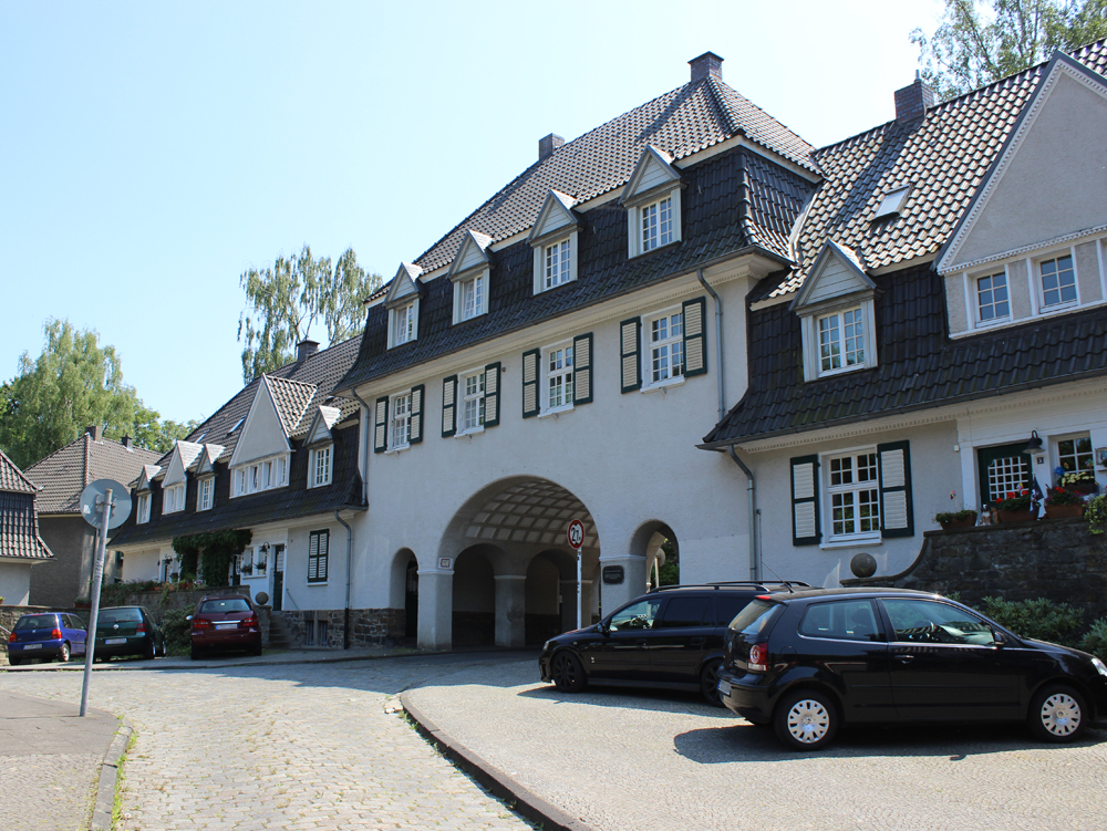 Einfamilienhaus mit Torbogen und Autos auf der Straße davor. 
