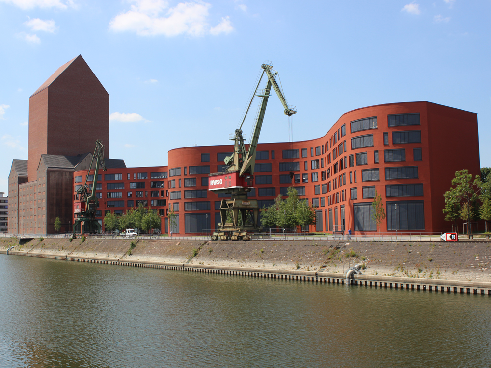 Landesarchiv NRW Rote moderne Gebäude am Wasser mit einem Kran im Vordergrund. Landesarchiv NRW, Innenhafen Duisburg