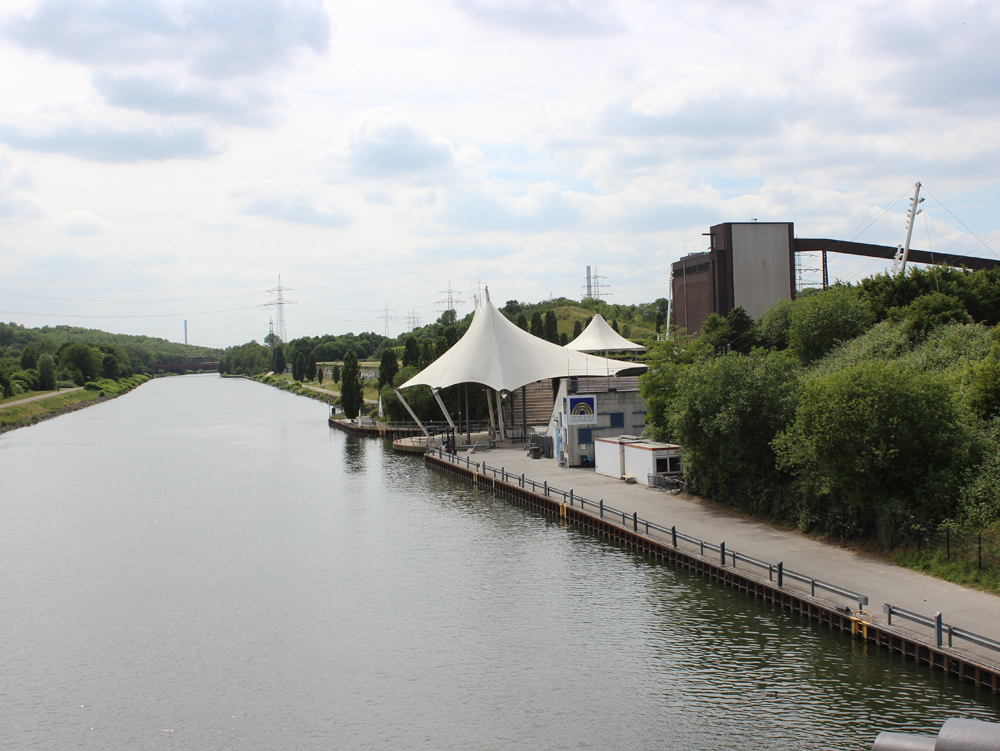 Amphietheater am Kanal Blick auf einen Kanal mit einem weißen Zeltdach und grüner Ufervegetation. Amphietheater am Rhein-Herne-Kanal, Nordsternpark Gelsenkirchen