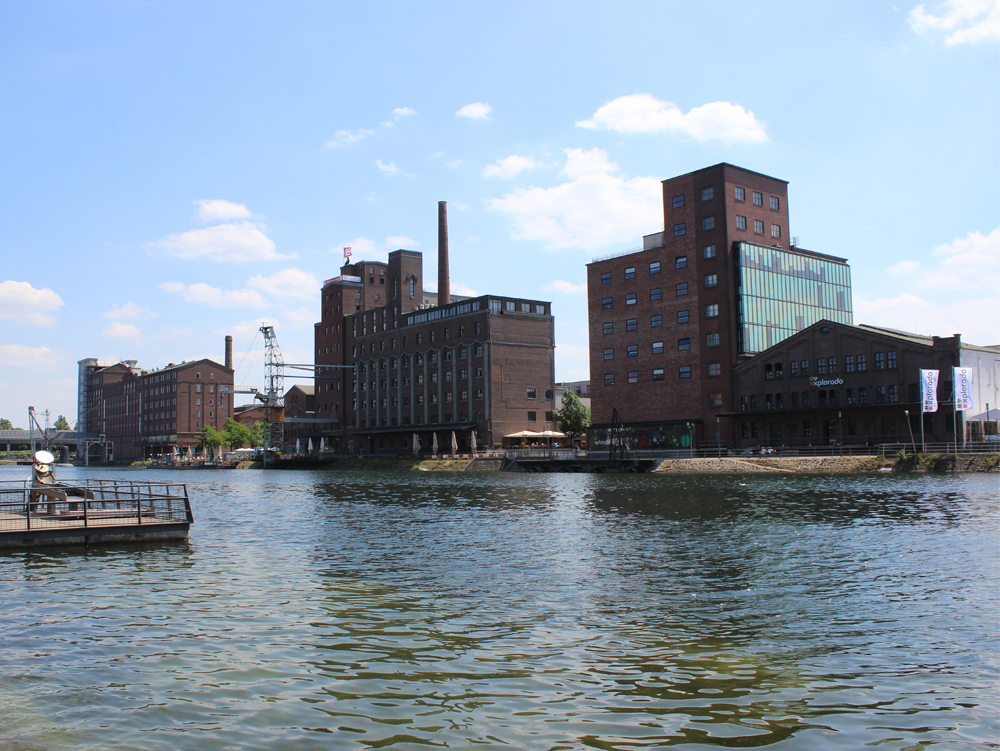 Wehrhahnmühle, Faktorei 21, Küppersmühle Industriegebäude am Wasserrand, klare Himmel und ruhige Wasseroberfläche.
Innenhafen Duisburg alte Speichergebäude
