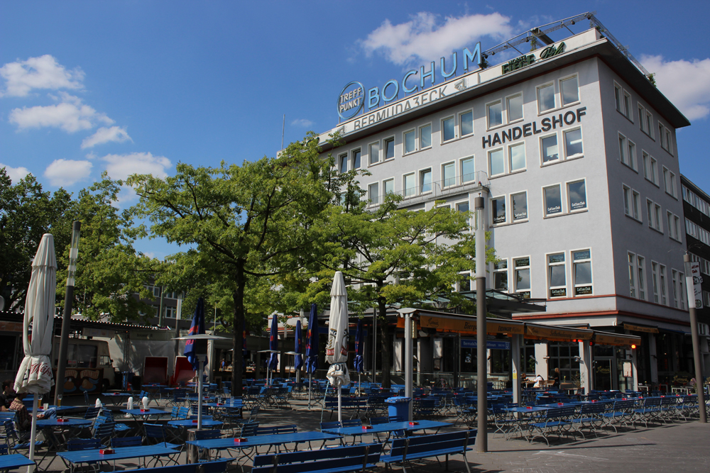Biergarten Bermudadreieck Blick auf ein Gebäude mit Außenrestaurant und grünen Bäumen im Vordergrund. Handelshof/Mandragora, Bochum