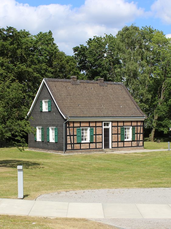 Fachwerkhaus mit grünem Fensterrahmen, umgeben von Bäumen und Rasenfläche. Stammhaus Krupp, Stadtrundfahrt Essen auf Ruhrdeutsch