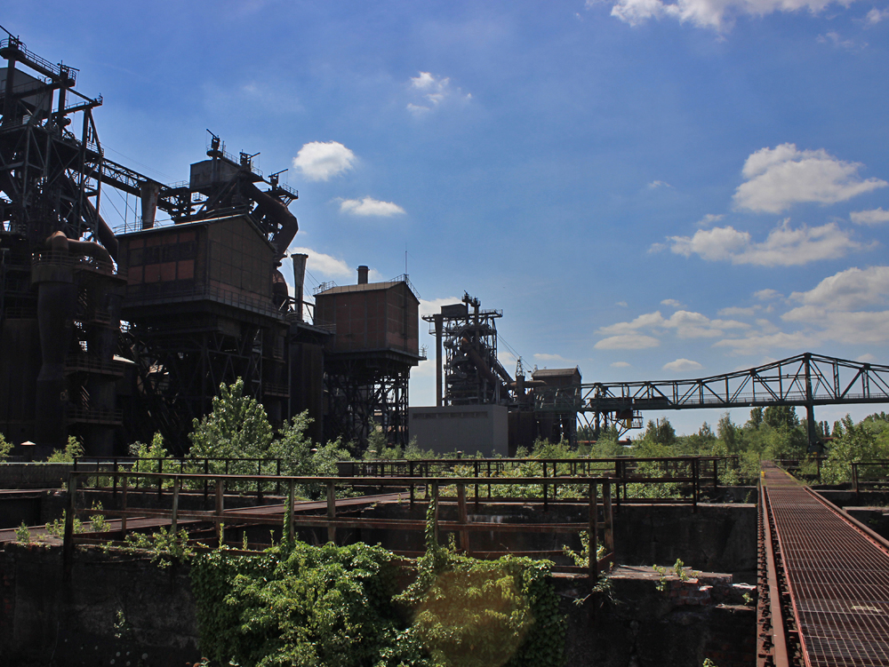 Landschaftspark Duisburg-Nord, Möllerbunker Verlassene Industrieanlage mit grüner Vegetation und aufragenden Gebäuden unter blauem Himmel.
Landschaftspark Duisburg-Nord, Möllerbunker
