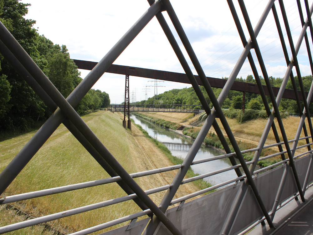 Emscherbrücke Blick durch ein Gitter über einen Fluss und eine bewaldete Uferlandschaft. Emscherbrücke Nordsternpark Gelsenkirchen