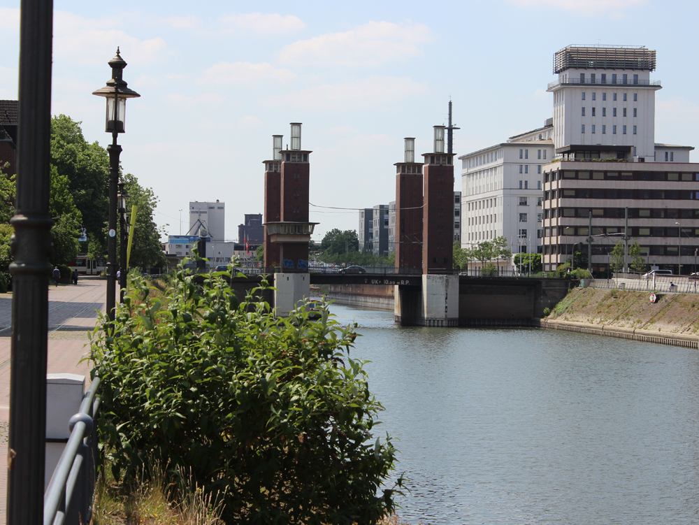 Schwanentorbrücke Blick auf einen Kanal mit Brücke, grüner Ufervegetation und modernen Gebäuden im Hintergrund. Schwanentorbrücke, Innenhafen Duisburg